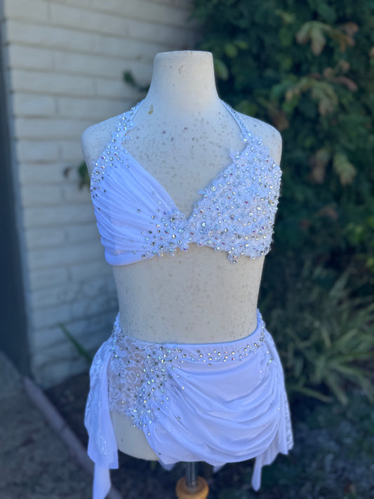 White beaded top and skirt dance set on a mannequin against a brick wall and plant background