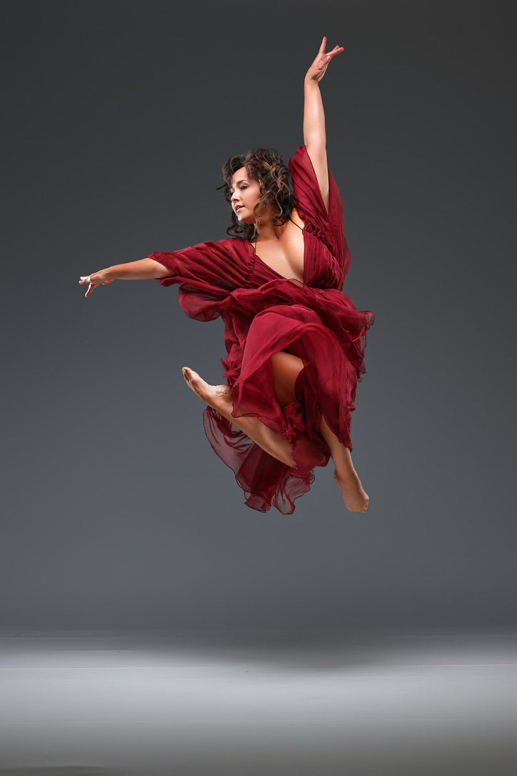Dancer in a red dress performing a jump against a gray background