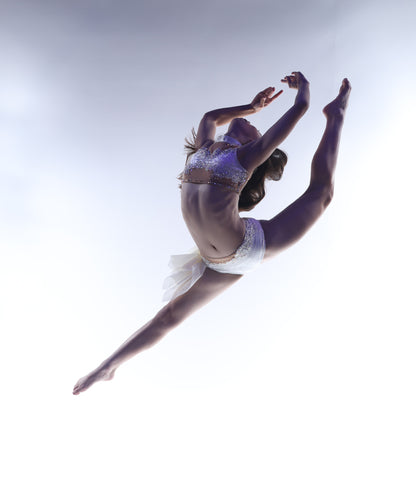 Dancer in mid-air against a light background wearing a custom ivory dance costume