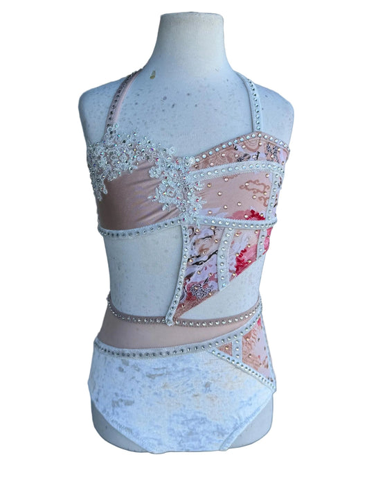 A multicolor dance costume displayed on a mannequin, featuring blush matte spandex with mesh, velvet, and lace fabrics in an asymmetrical design with rhinestone embellishments.